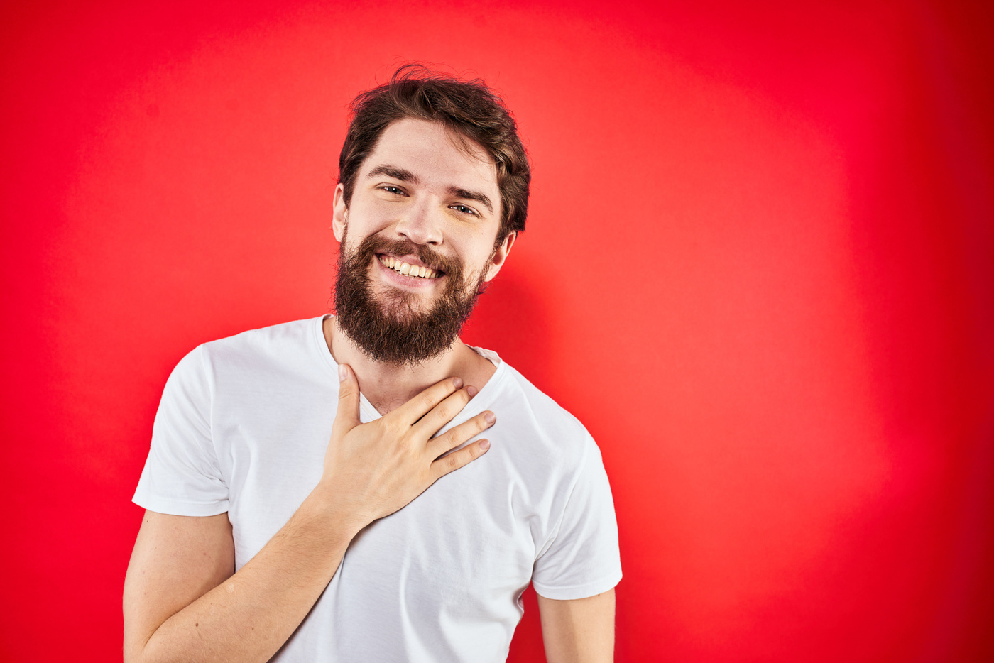 A Man in a White T-Shirt with a Beard Gestures with His Hands Emotions Red Background